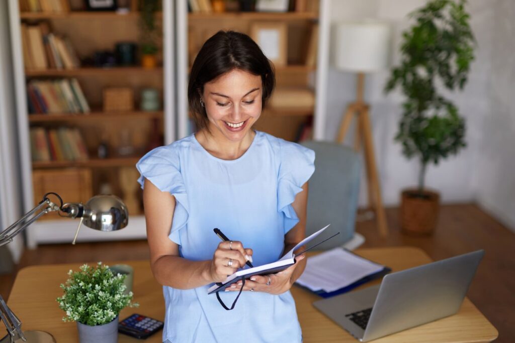 Person schreibt Notizen am Schreibtisch und plant eine Wohnungsaufloesung Neuss, mit Laptop, Unterlagen und Buerozubehoer.