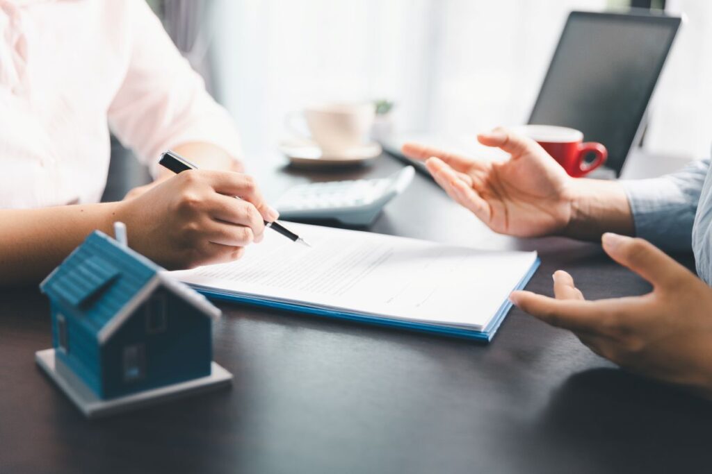 Zwei Personen besprechen Unterlagen zu einer Wohnungsaufloesung Neuss, mit Stift, Dokumenten und kleinem Hausmodell auf dem Tisch.