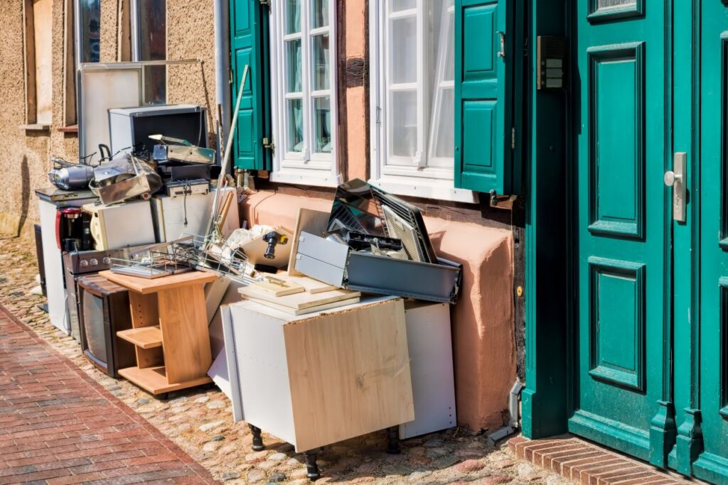 Abgestellte Moebel, Elektrogeraete und Hausrat vor einer Haustuer nach einer Wohnungsaufloesung Neuss, bereit zur Entsorgung und Abholung.